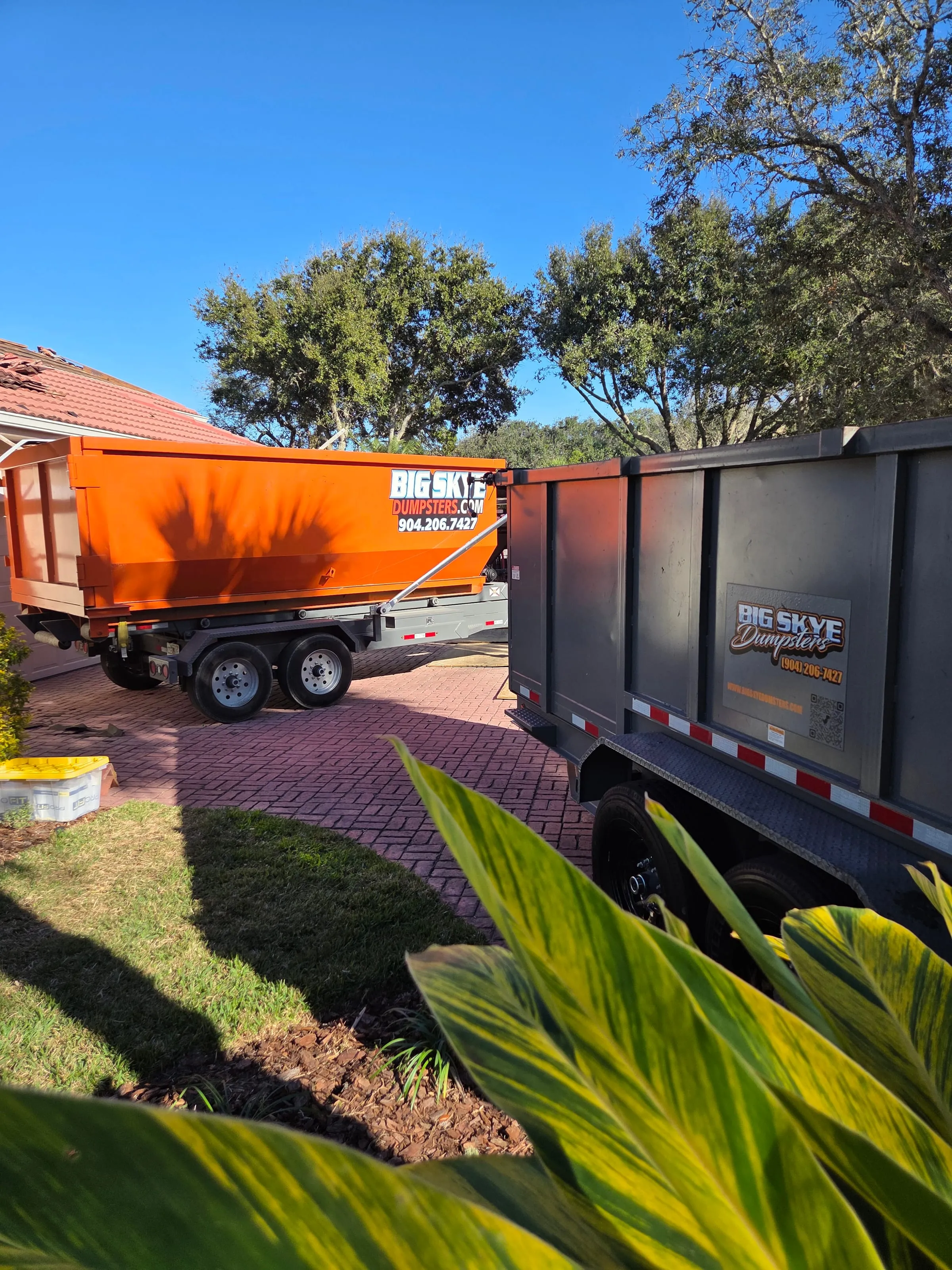 Orange Big Skye dump trailer and roll-off on a red paver driveway