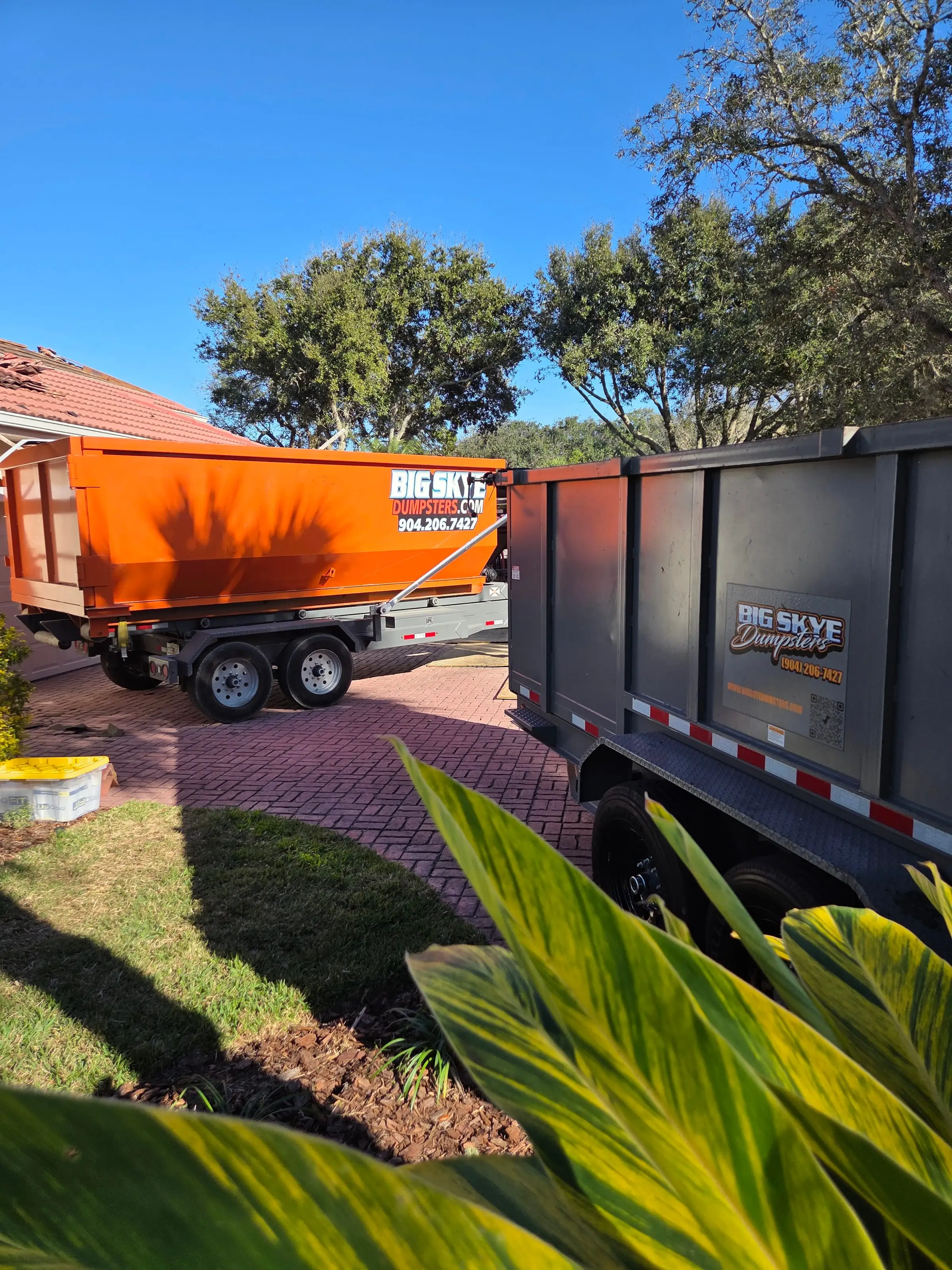Orange Big Skye dump trailer and roll-off on a red paver driveway