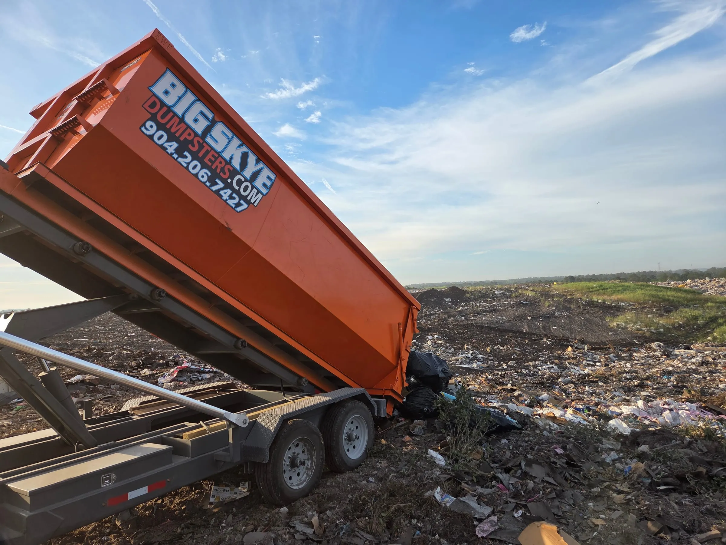 Orange Big Skye dump trailer tilted up to unload at the landfill